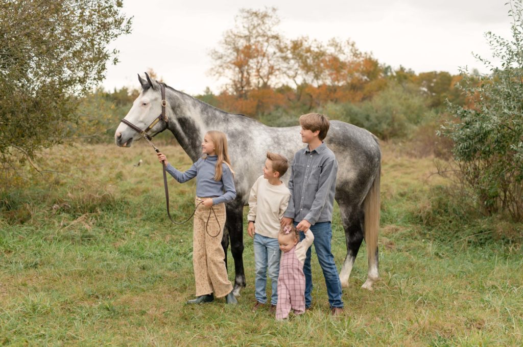 Family photos with your horse — a group of four children smile as they stand next to their ash gray horse