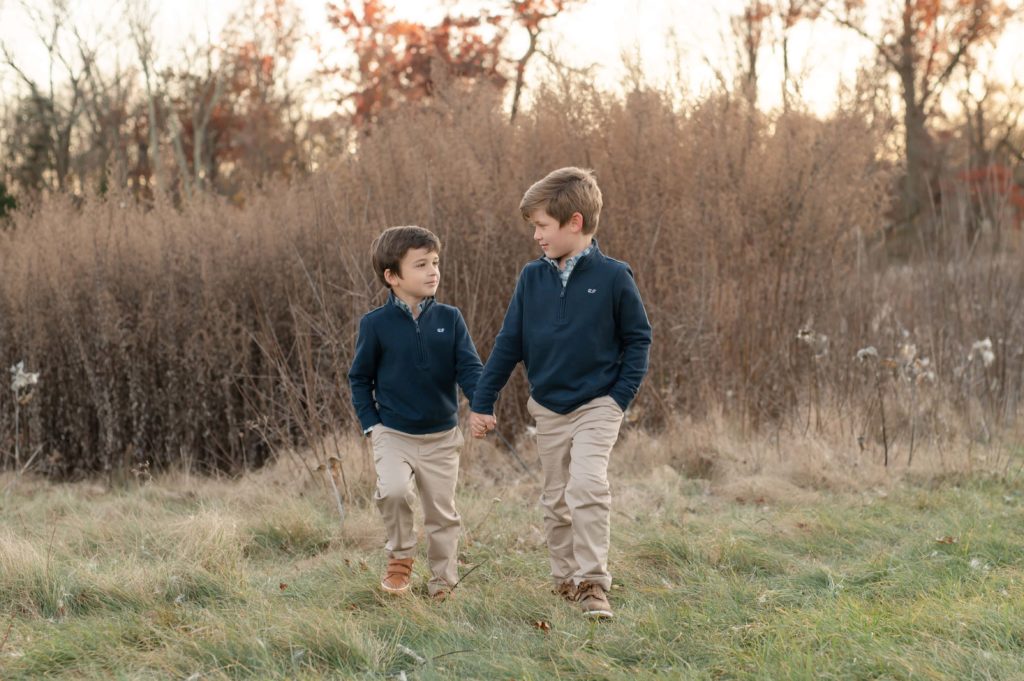 Family photos in navy with two brothers holding hands in the field at golden hour