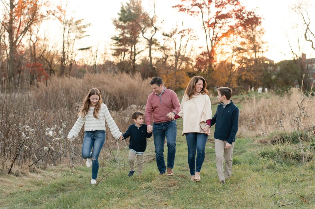 Massachusetts family photos at golden hour with the family holding hands walking through a field
