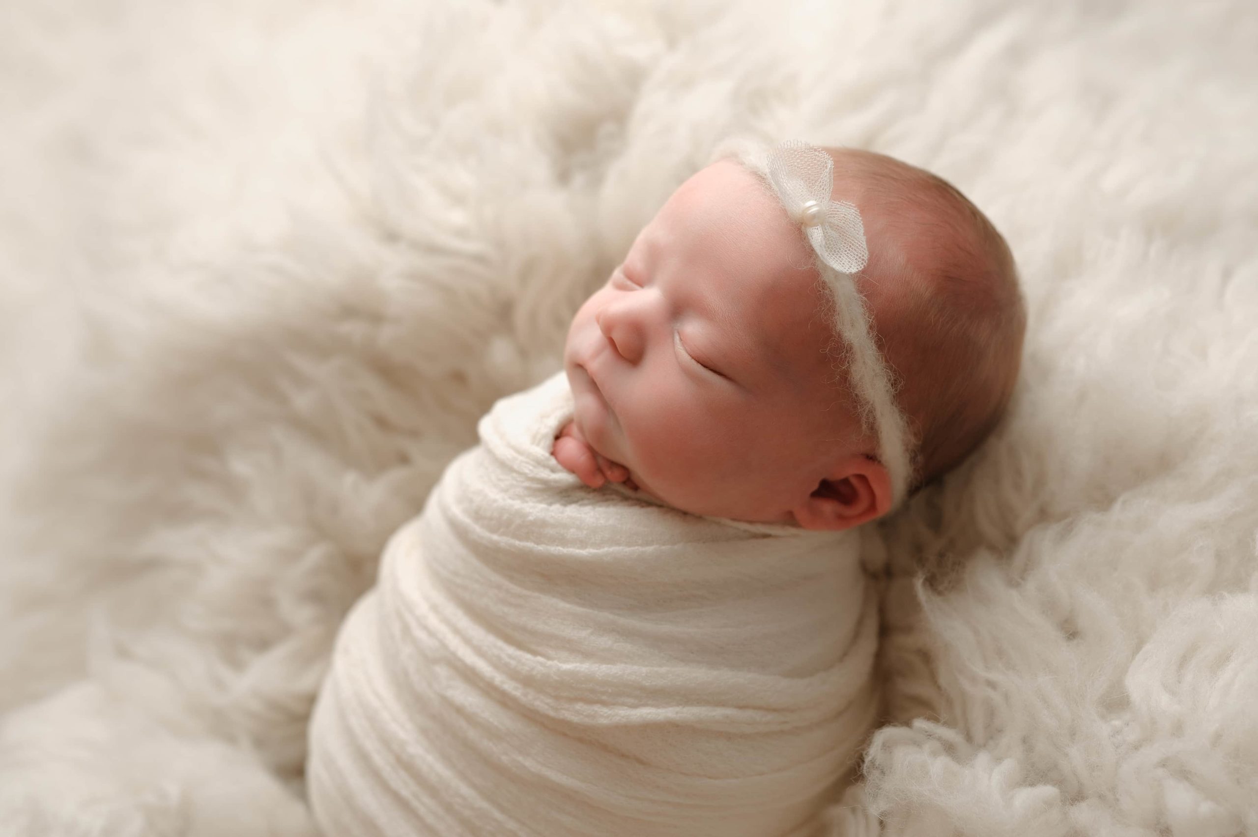 Newborn photo in faux wool and swaddled in a white blanket