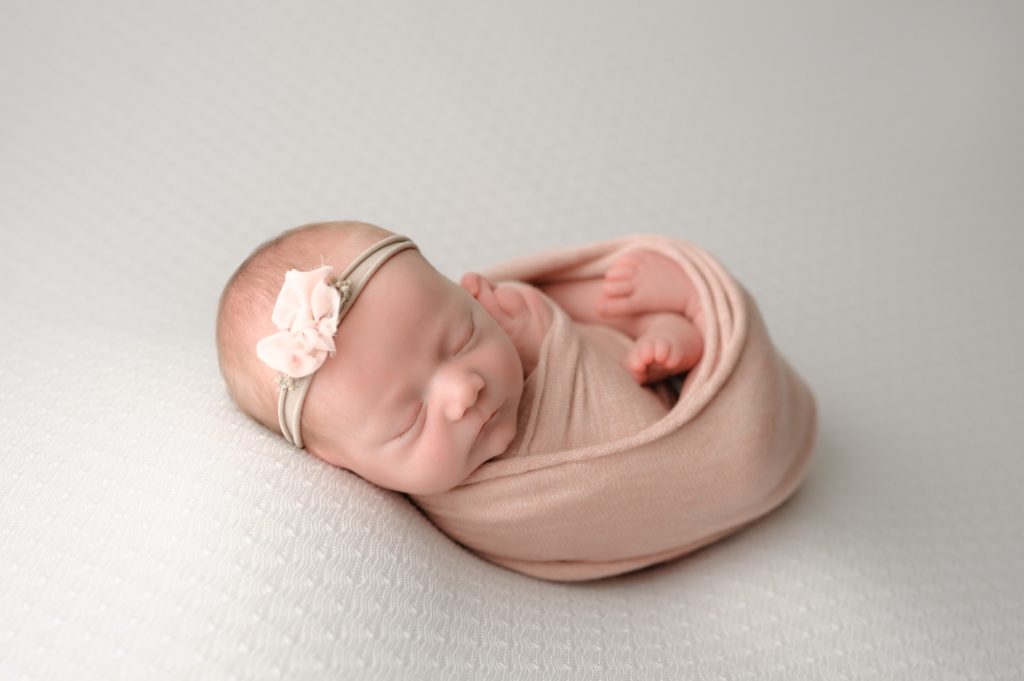 Swaddled newborn photo with a headband and simple beige background