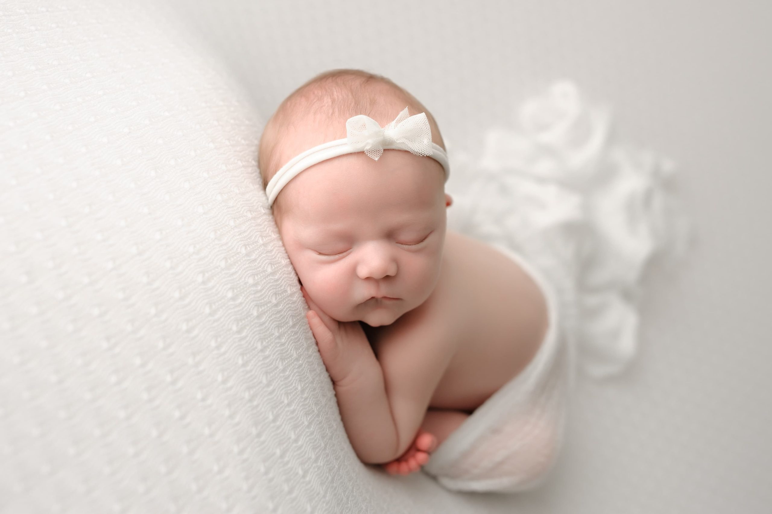 Newborn photo with baby sleeping on its arms while wearing a headband