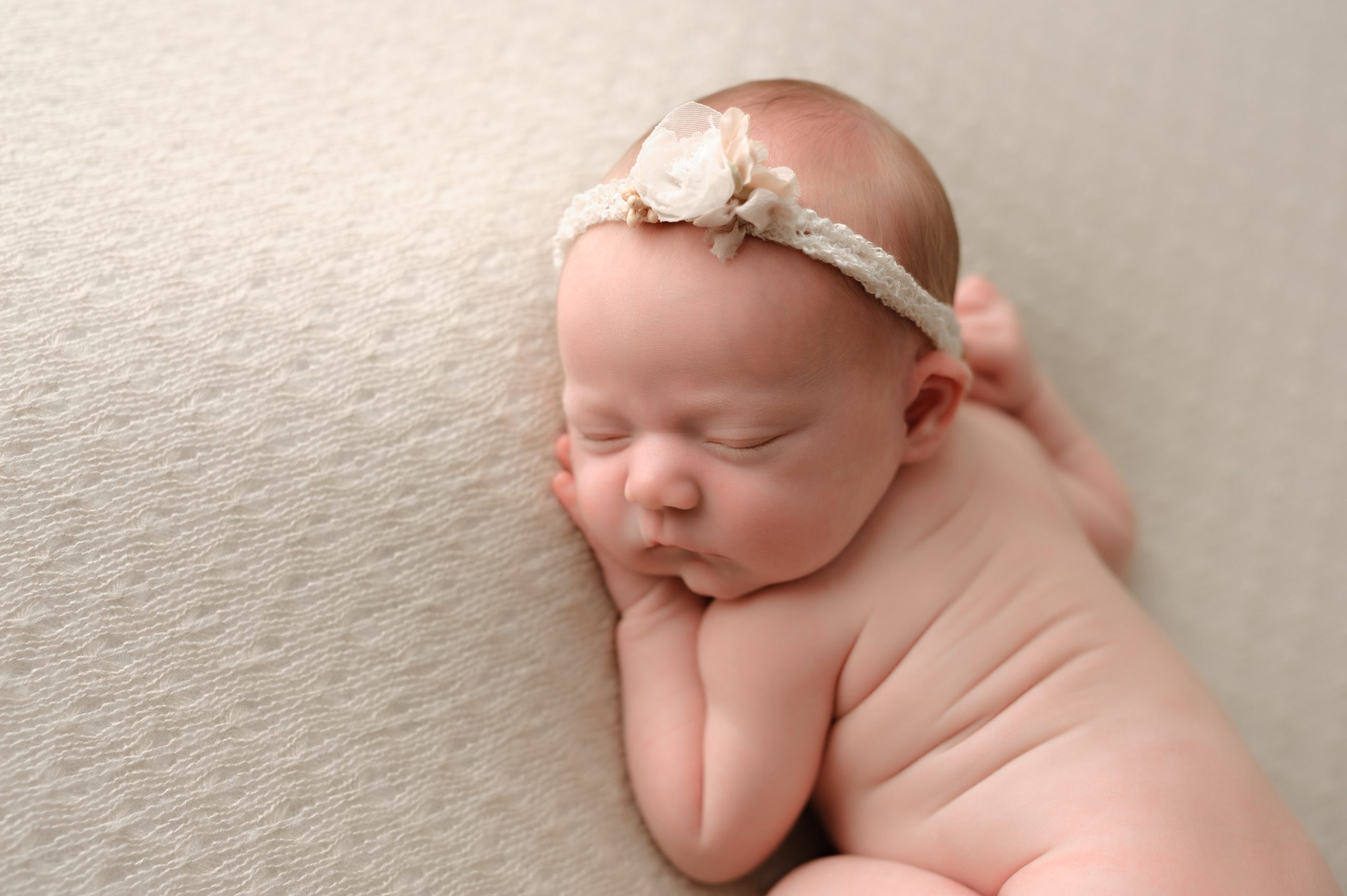 Newborn photo with a beige/ivory background and a simple headband