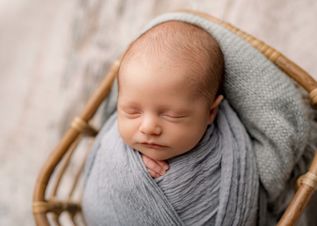 Newborn swaddled in a stone blue blanket sleeping in a basket